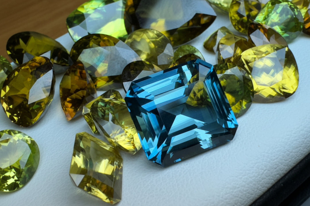 high-quality collection of emerald-cut blue indicolite tourmaline and radiant-cut yellow gemstones on a white display