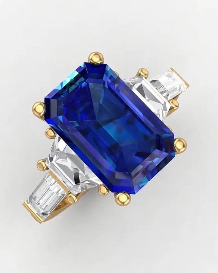 A luxury 18k gold ring featuring a large emerald-cut blue sapphire center stone, flanked by tapered baguette diamond side stones on a clean white background