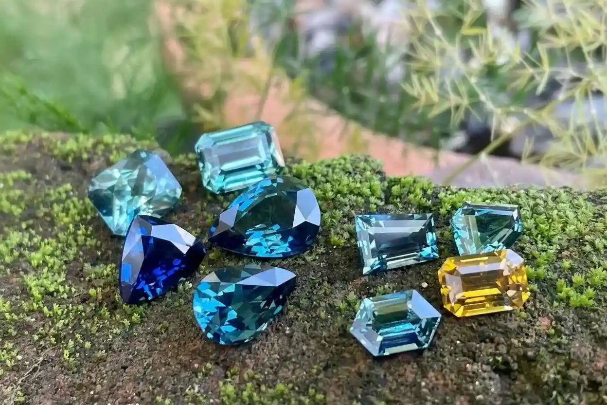 Collection of colorful gemstones on a natural surface with blurred greenery in the background