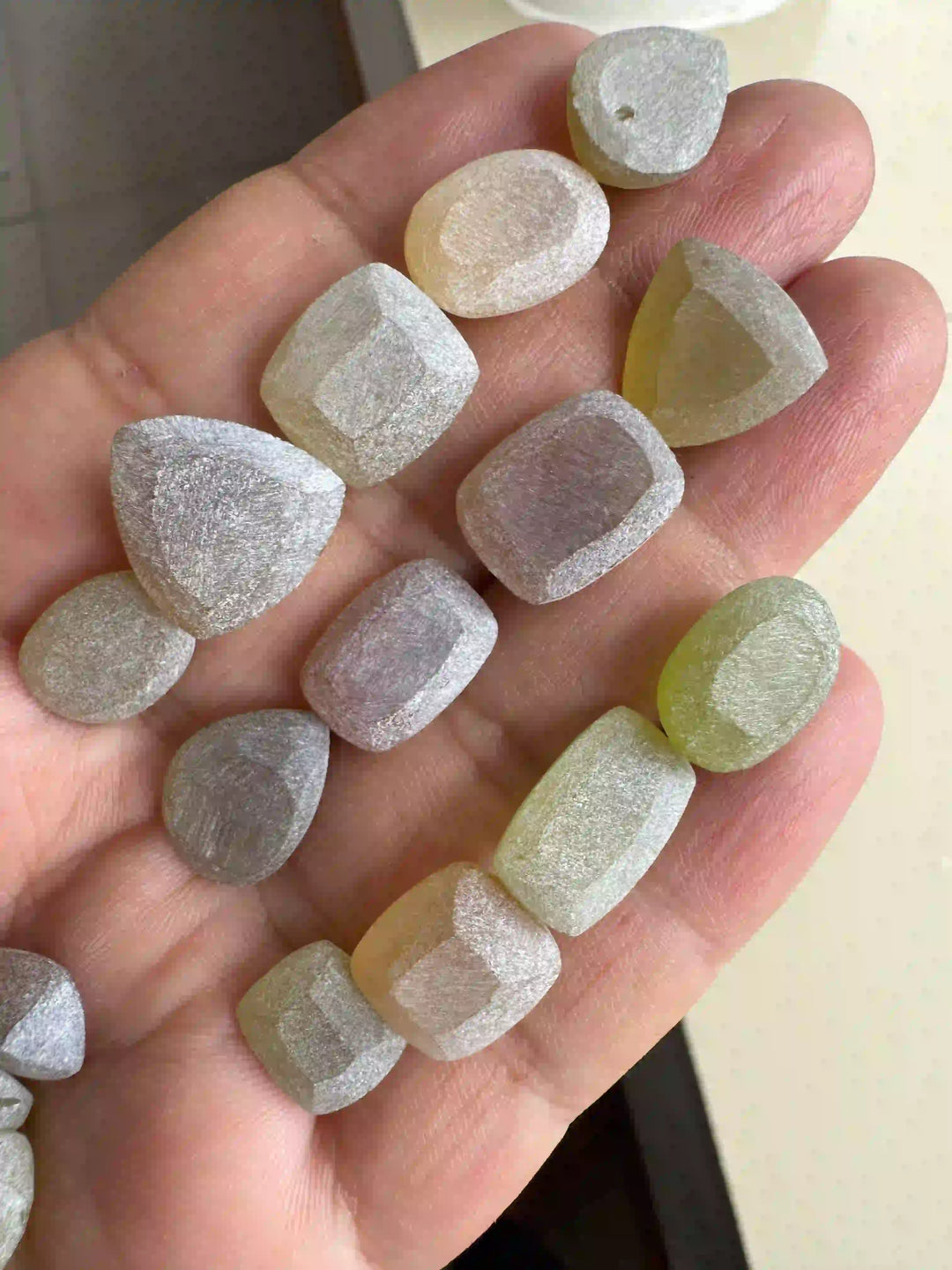 A hand holding a collection of large, translucent moonstones with a soft blue and white adularescence, featuring cushion and pear-shaped cuts