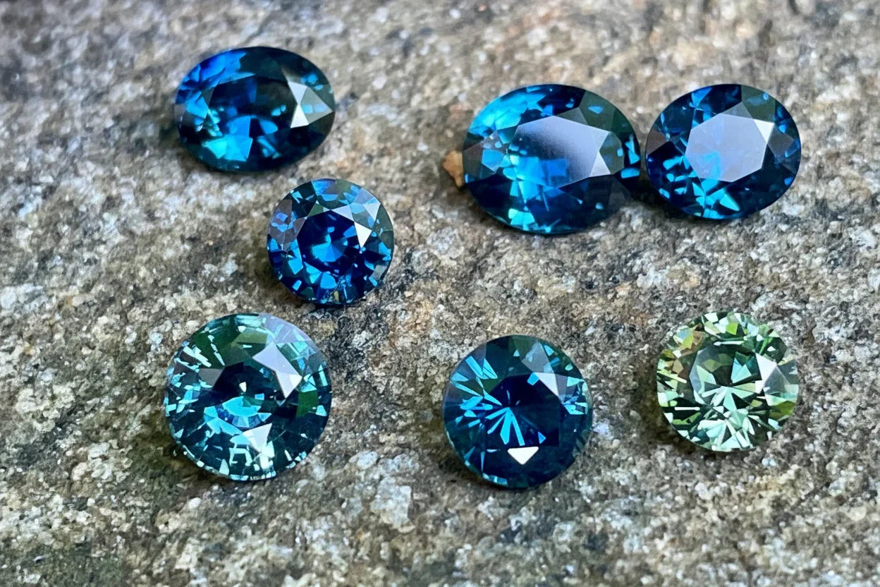 collection of natural round-cut teal and blue sapphires displayed on a grey stone surface
